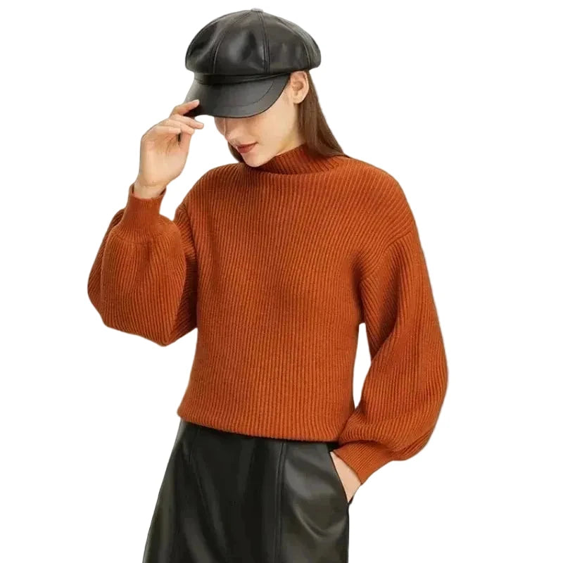 A woman wearing a ribbed orange-brown mock neck sweater, a black leather cap, and black leather pants, posed against a light gray studio background with the brand name AMII in the top left corner.