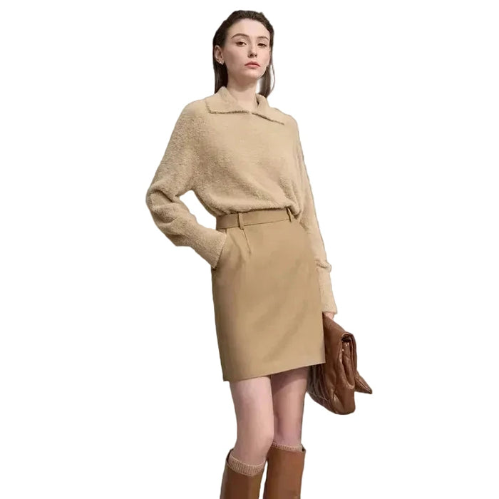 Woman wearing a beige outfit with a skirt and sweater against a plain background